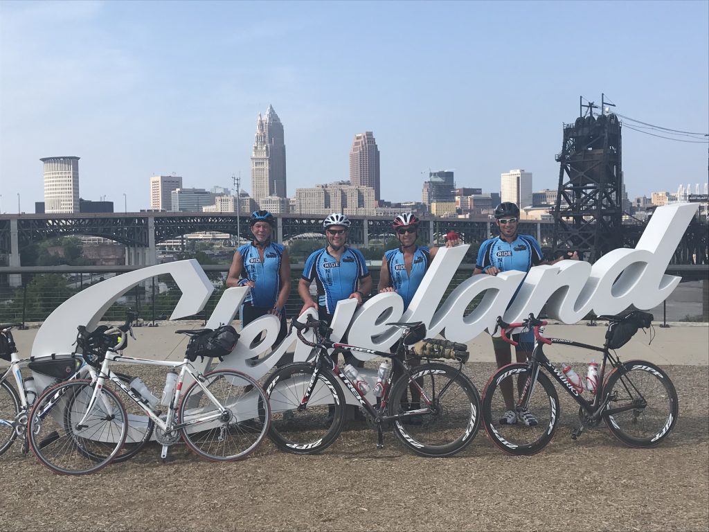 Four men standing in front of a Cleveland sign with bikes