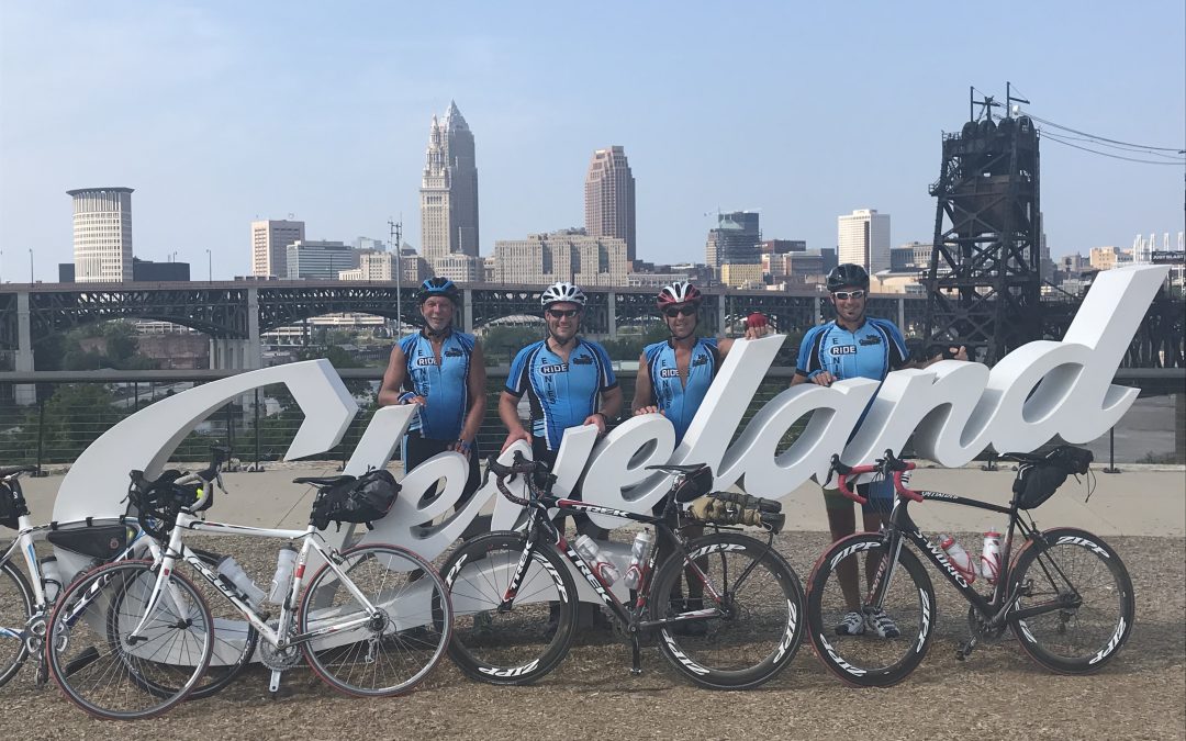Four men standing in front of a Cleveland sign with bikes